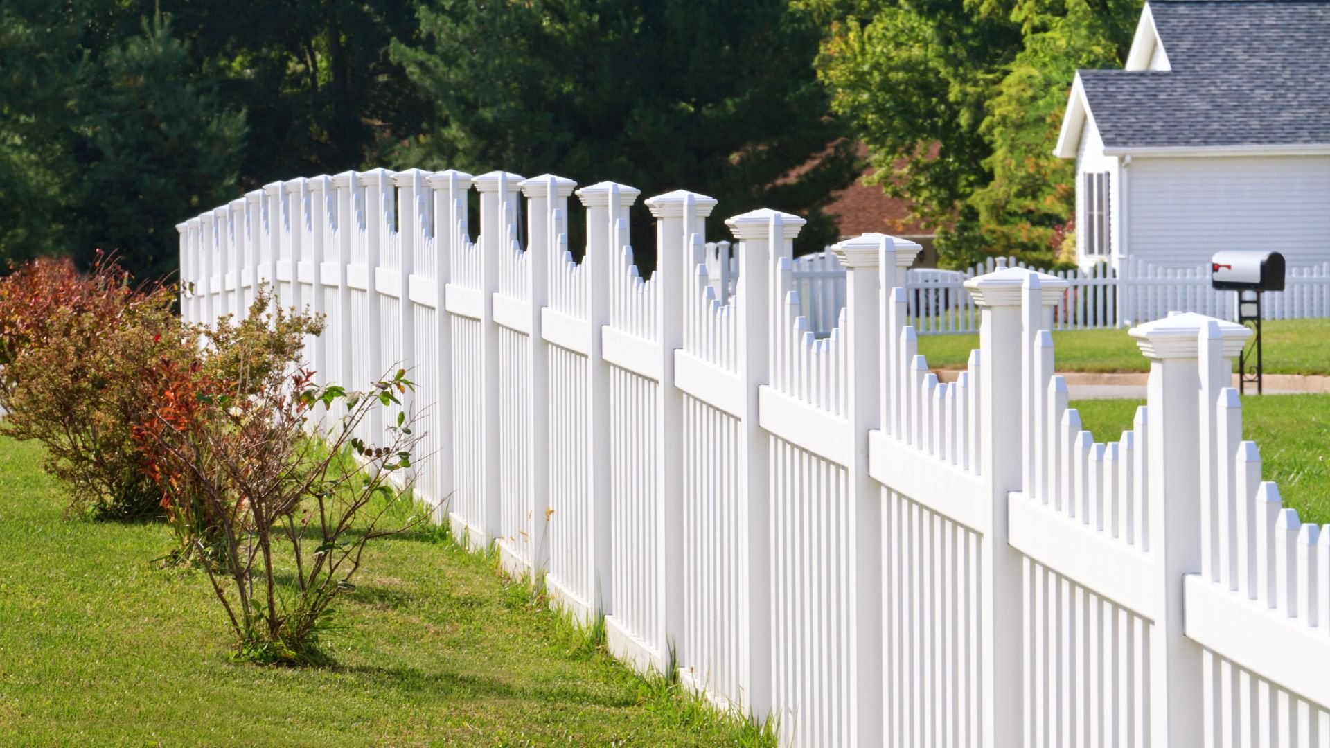 White picket fence along green lawn with house and trees in background