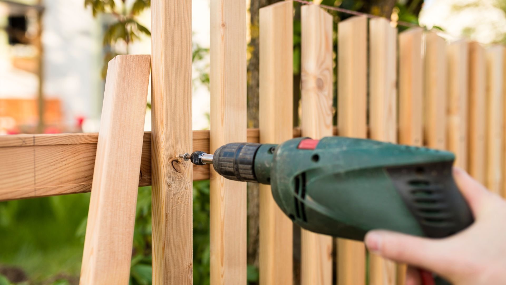 Drilling wooden fence post with green cordless power drill outdoors