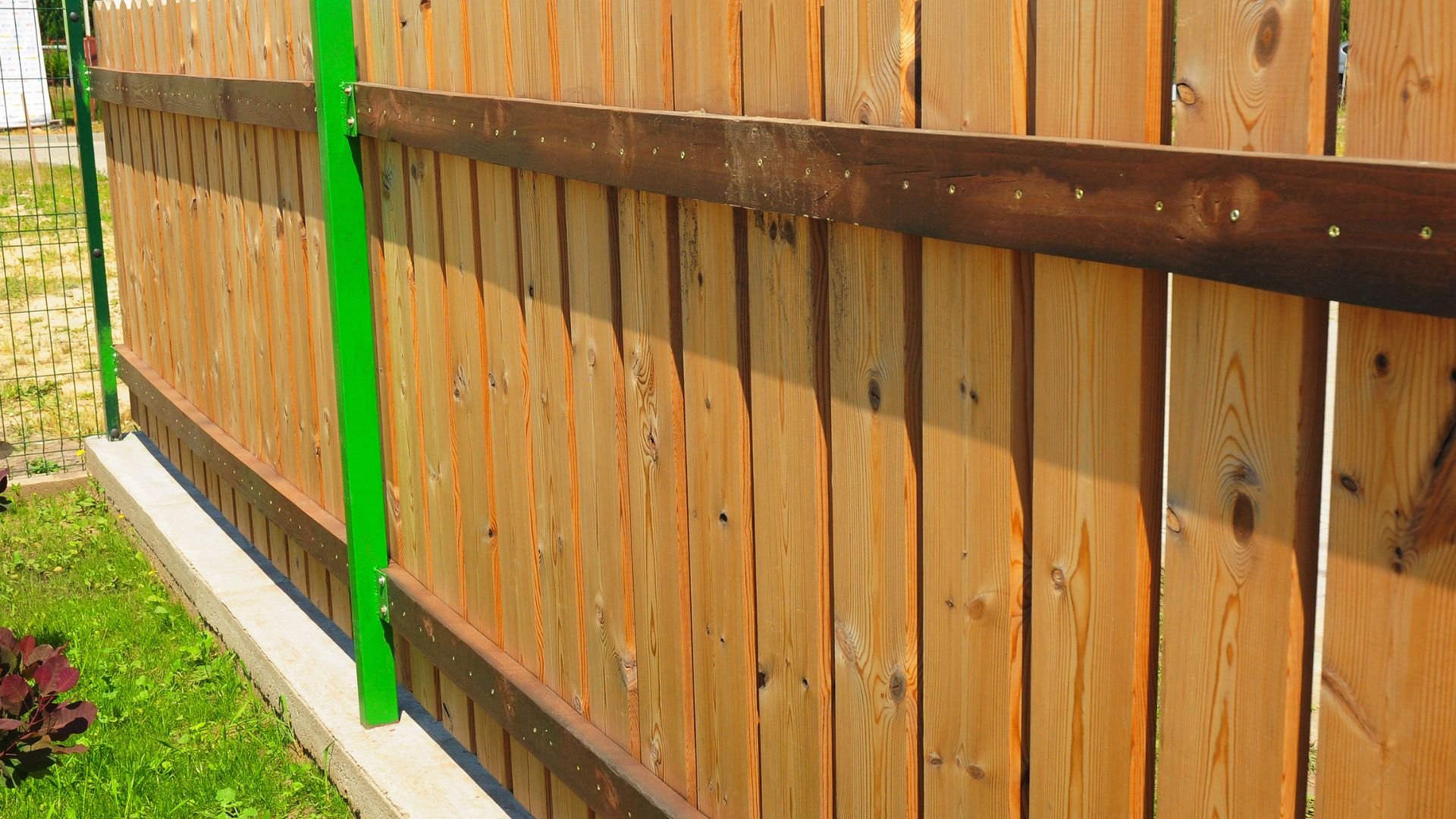 Wooden fence with vertical planks and green metal post