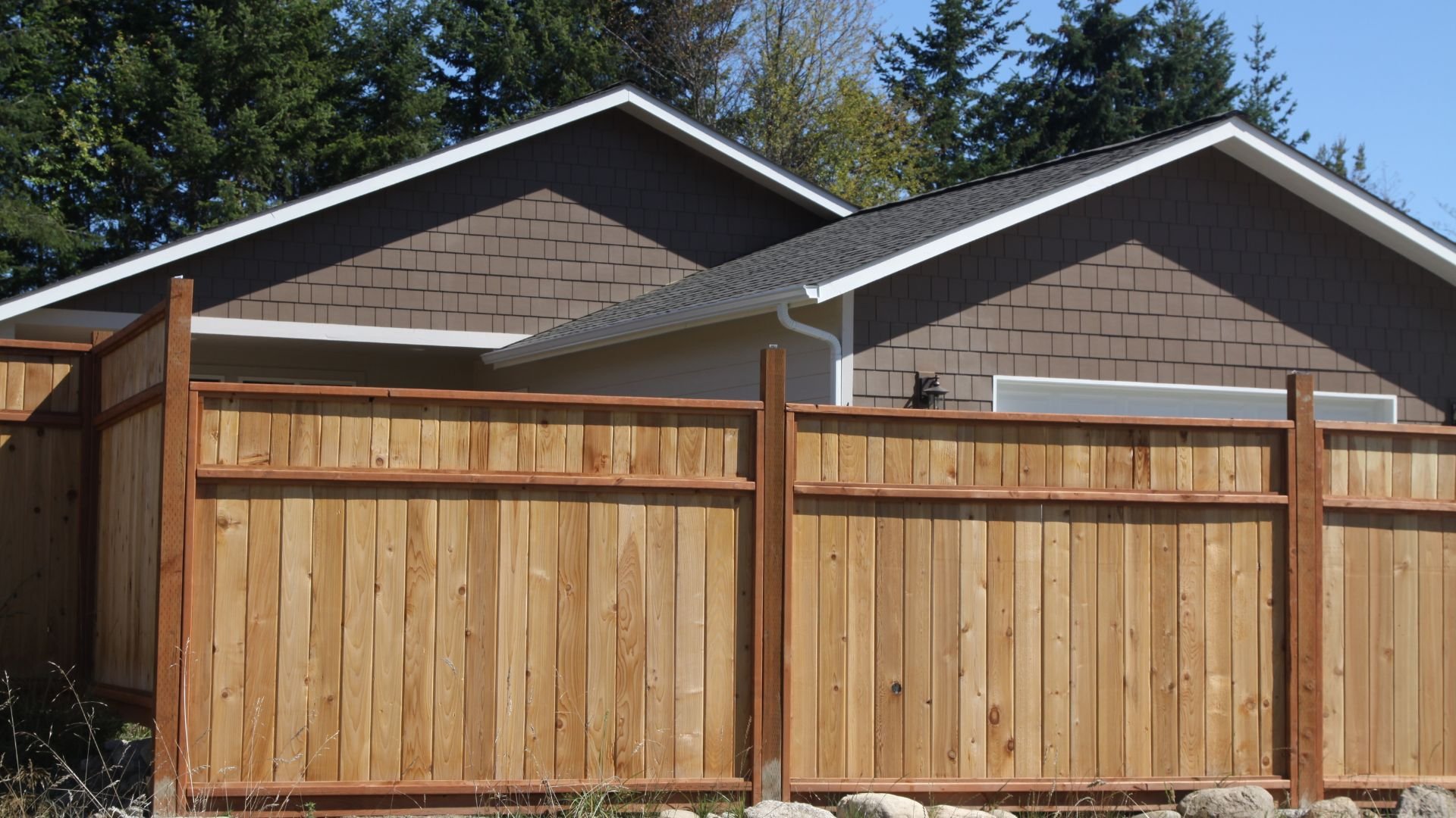 Wooden fence in front of a house with trees in the background